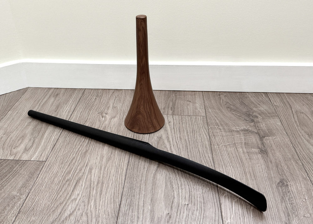 Black cylindrical shoehorn and wooden stand on a wooden floor.