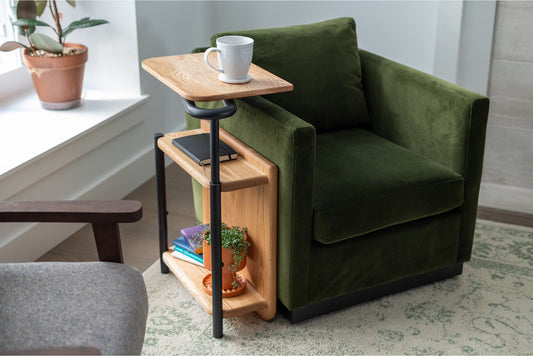 The Corbel Adjustable Side Table in oak with black hardware sitting beside a green chair.