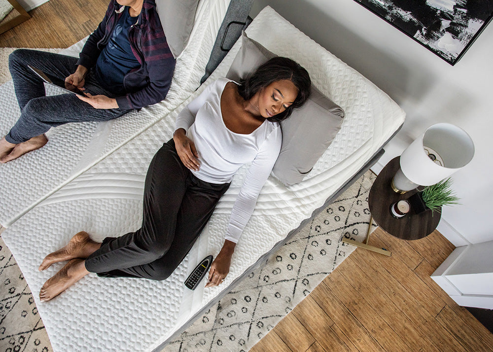 Two people lying on a mattress in a room with a rug and small table.