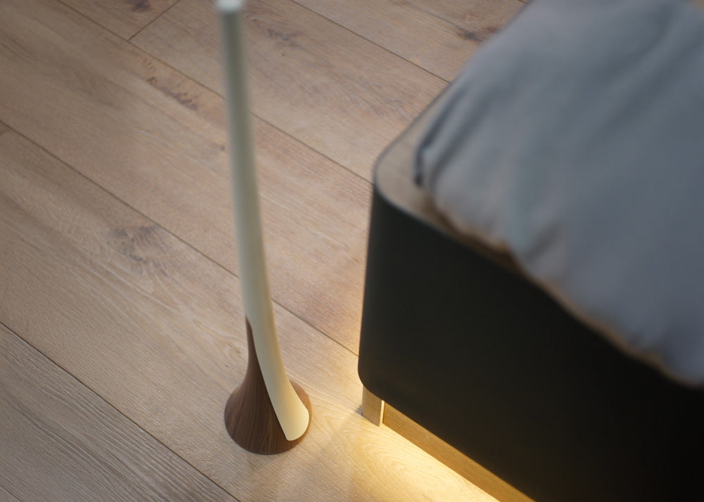 white and walnut shoehorn on a wooden floor next to a bed with a gray pillow