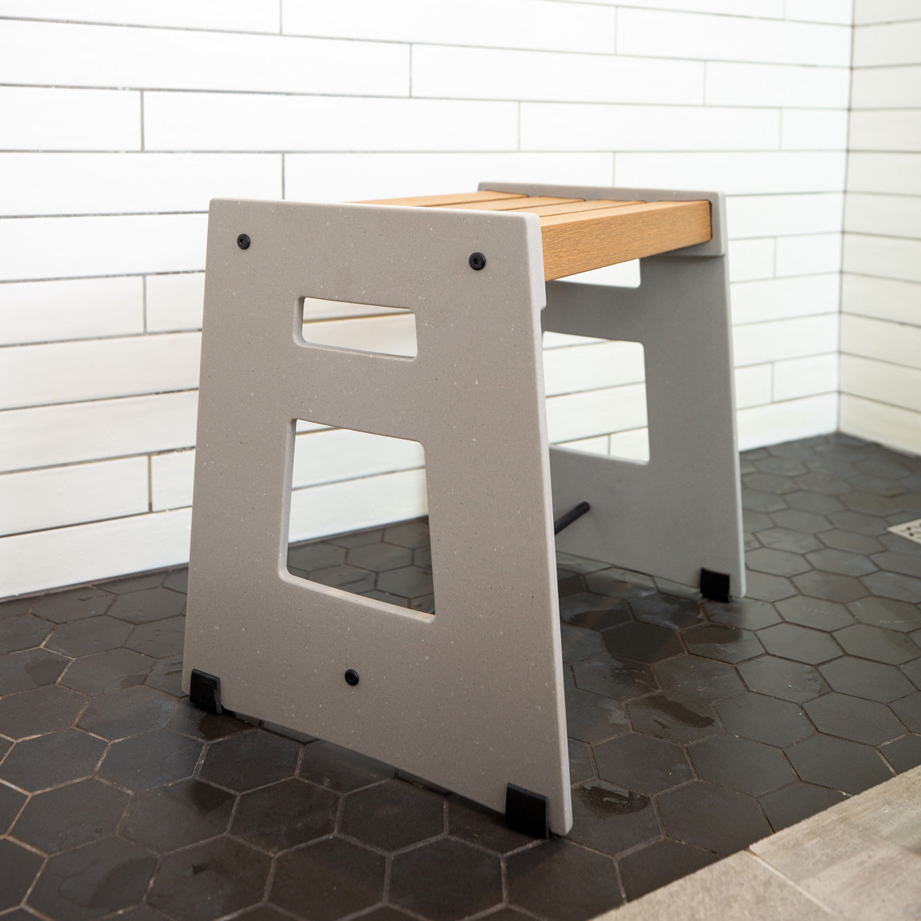 Lotic Shower Seat in concrete grey sitting in a white walled shower with black tile floor.