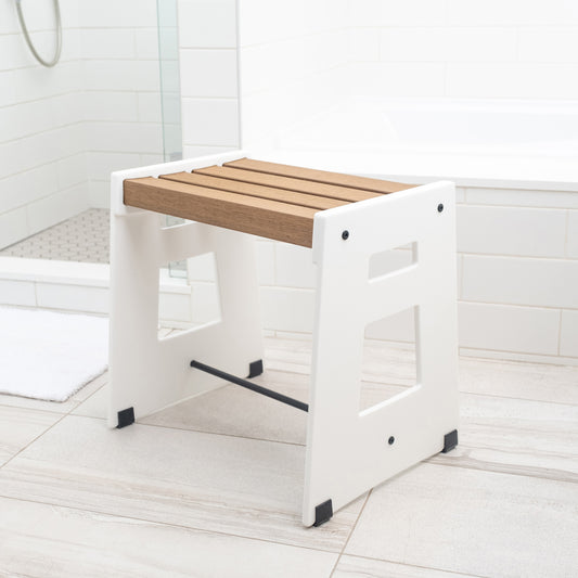The Lotic Shower Seat in white sitting on the floor of a bathroom.