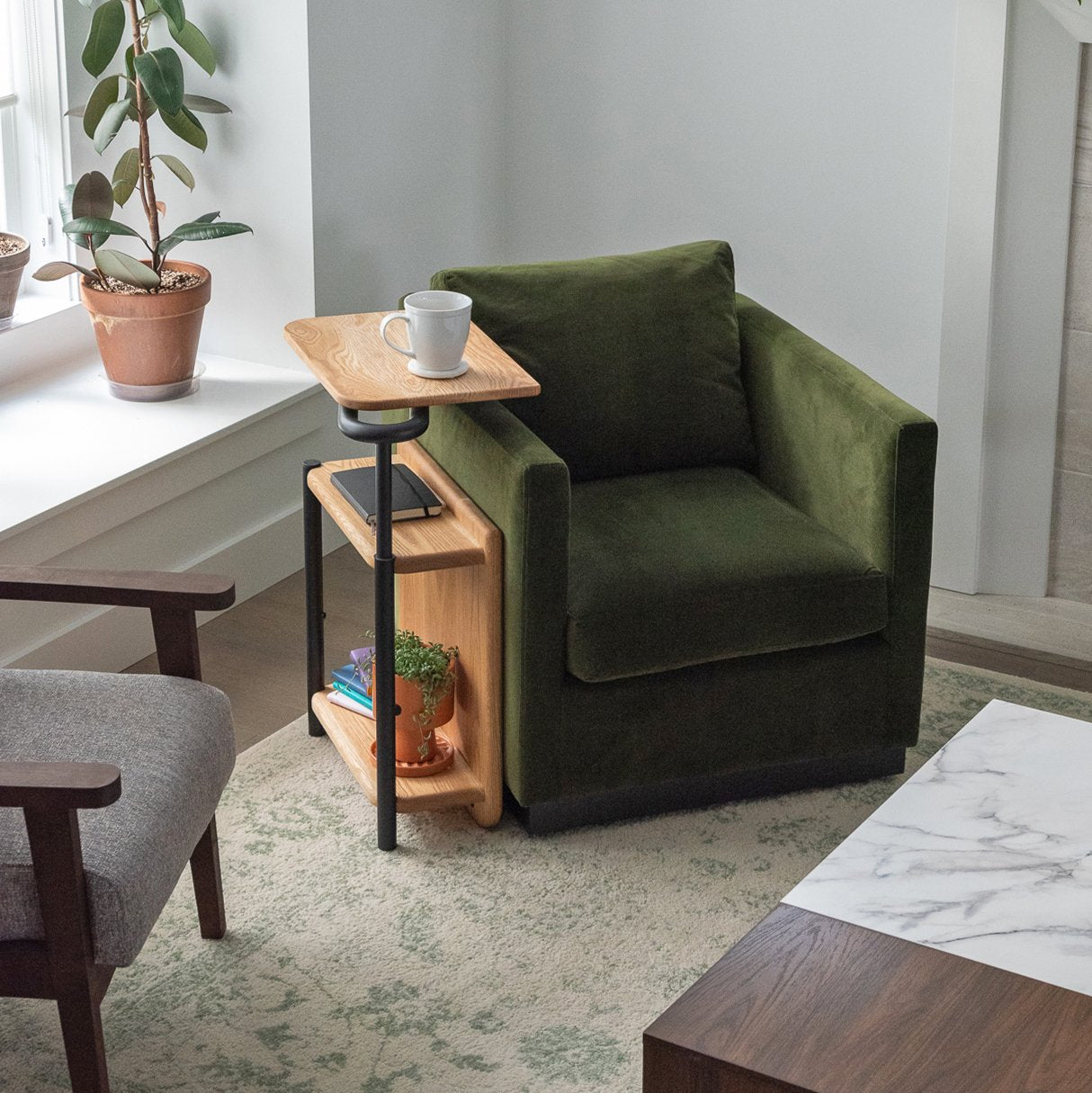The Corbel Adjustable Side Table in oak with black hardware sitting beside a green chair.