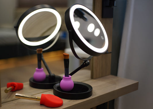Two round mirrors with LED lights on a wooden surface with makeup items.