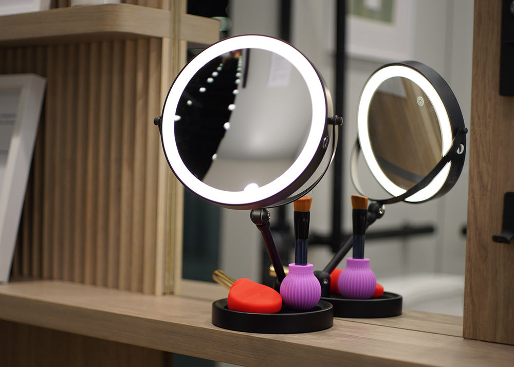 Two round makeup mirrors with LED lights on a wooden surface.