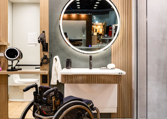 Wheelchair in a modern bathroom with a large round mirror and an adjustable vanity.