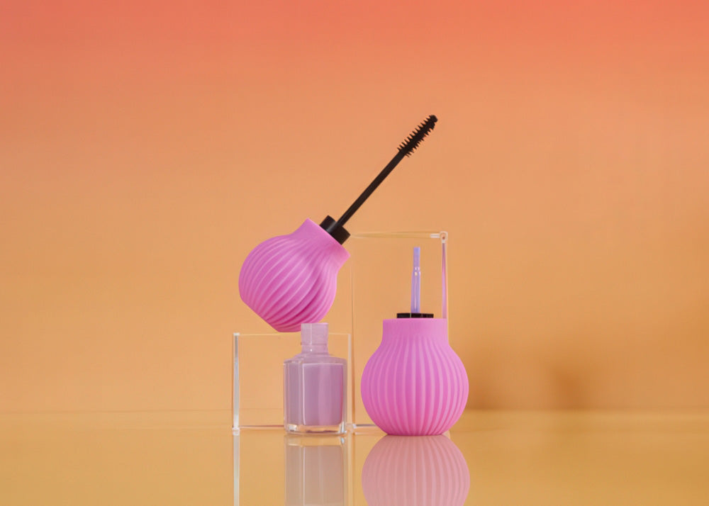 Pink makeup grippers with a black mascara wand in one and a nail polish brush in the other on an orange gradient background