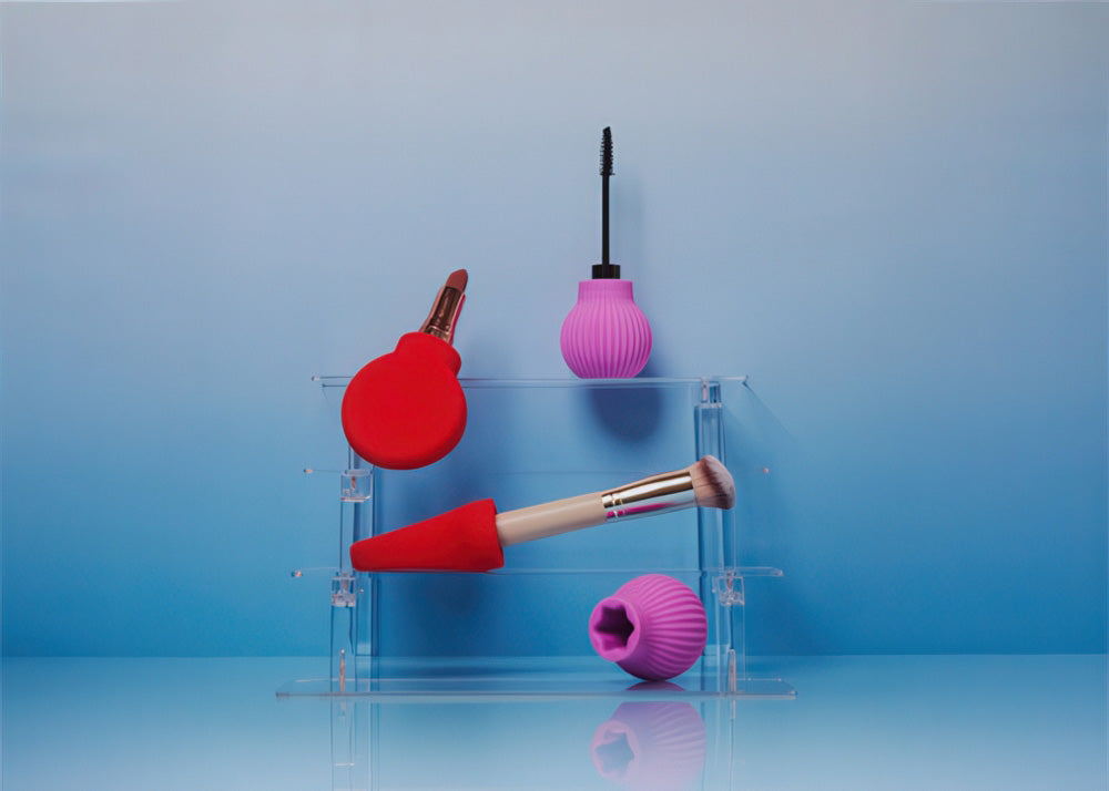 Makeup brushes with red and pink silicone grippers on a clear stand against a blue background