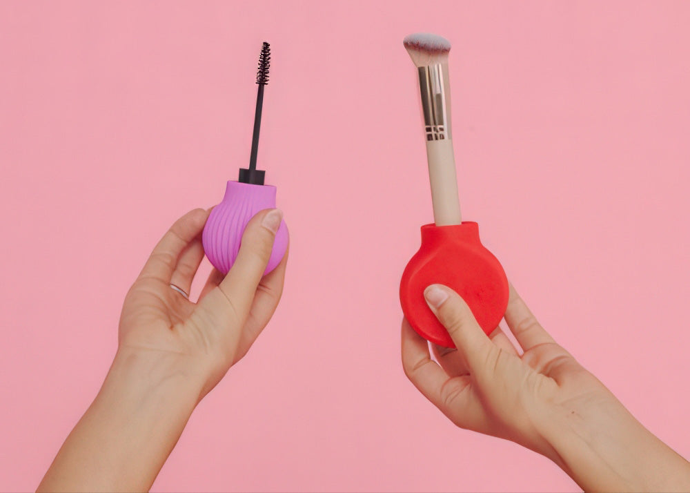 Two hands holding a pink and a red makeup tool against a pink background