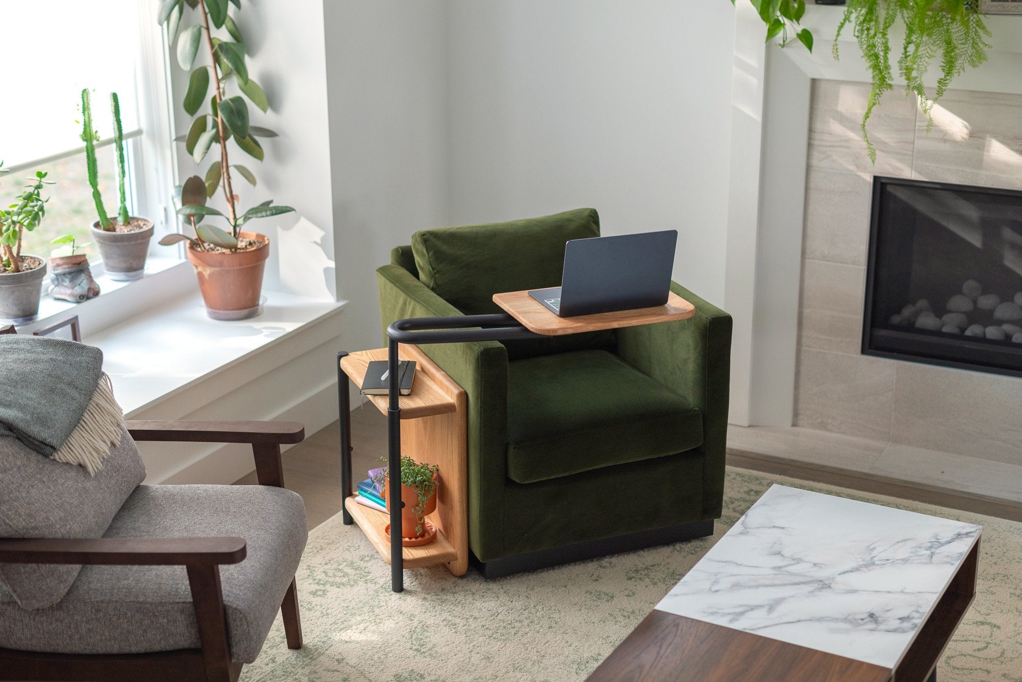 The Corbel Adjustable Side Table in oak with black hardware sitting beside a green chair.