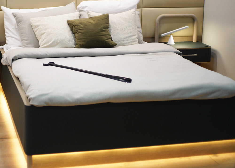 Black dressing stick lying on a bed with grey sheets and a dark green frame
