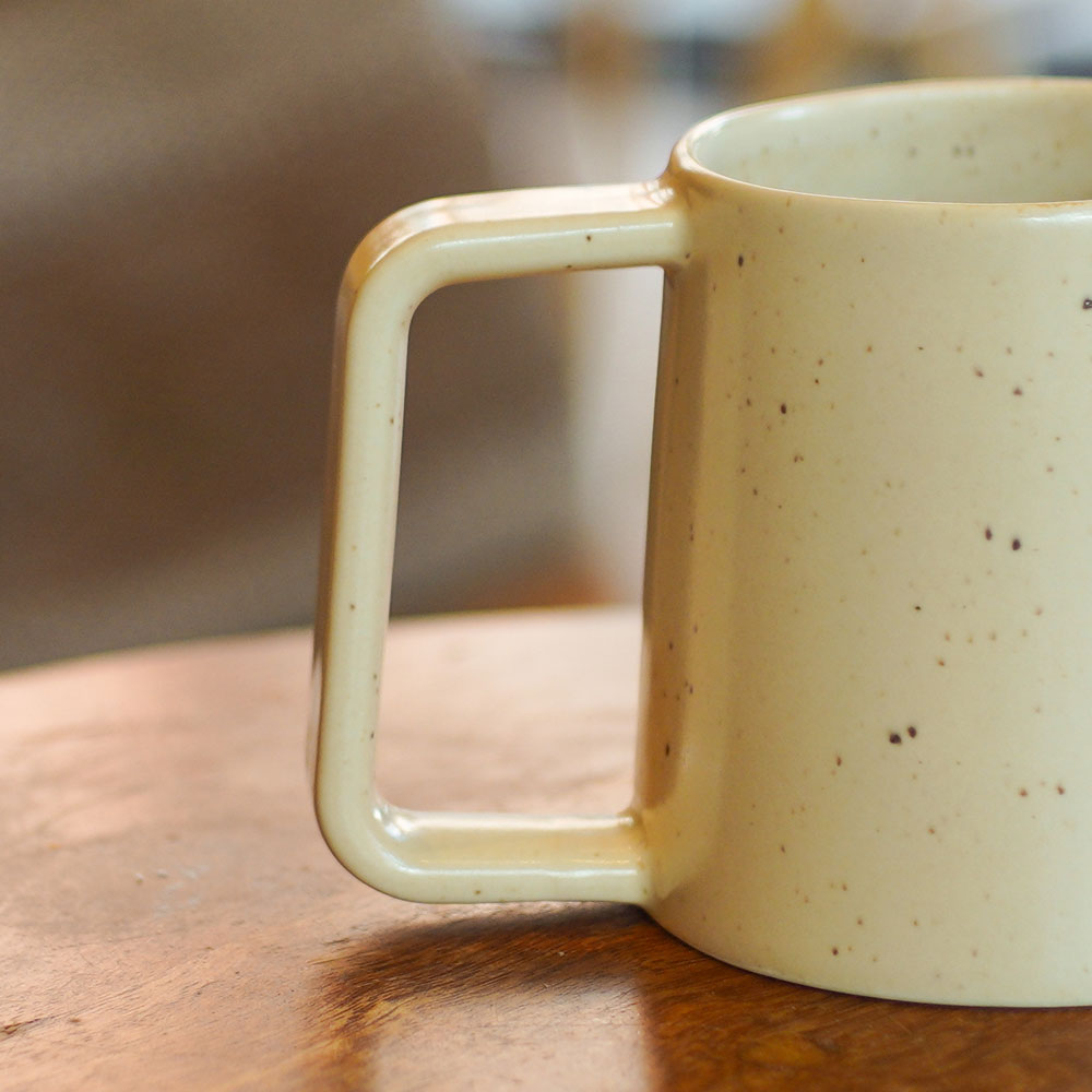 Large handle detail on a speckled beige mug on a wooden surface with a blurred background