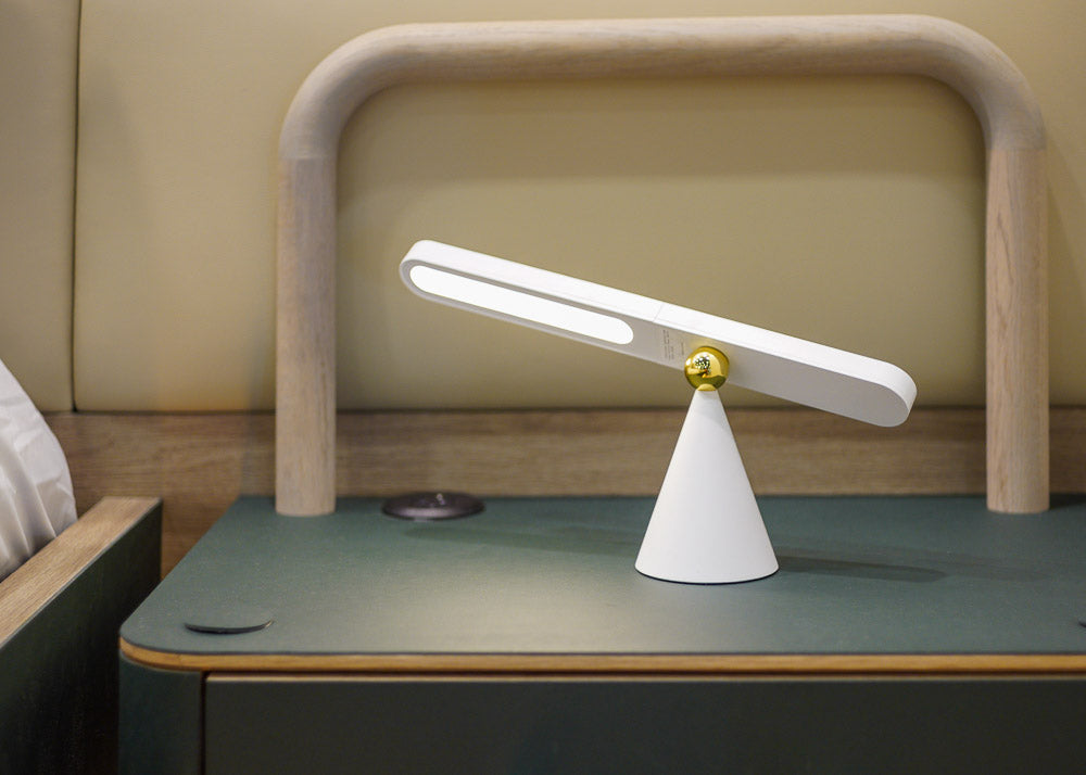 Modern desk or bedside lamp with a white base and gold accent on a green surface.