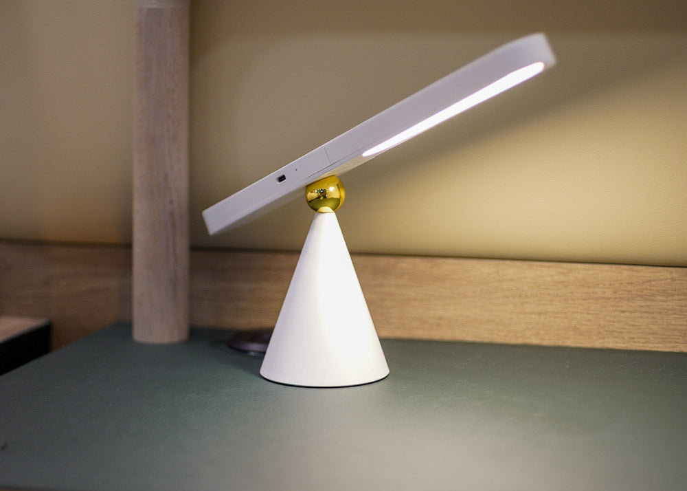 Modern desk lamp with white base and gold accent on a wooden surface