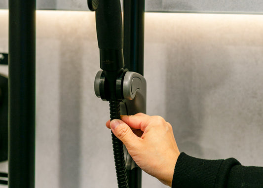 Hand moving a black shower hose with two fingers using an easy adjust shower head holder against a neutral background