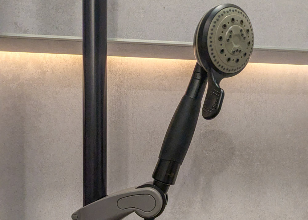 Handheld shower head attached to a shower arm against a neutral wall.