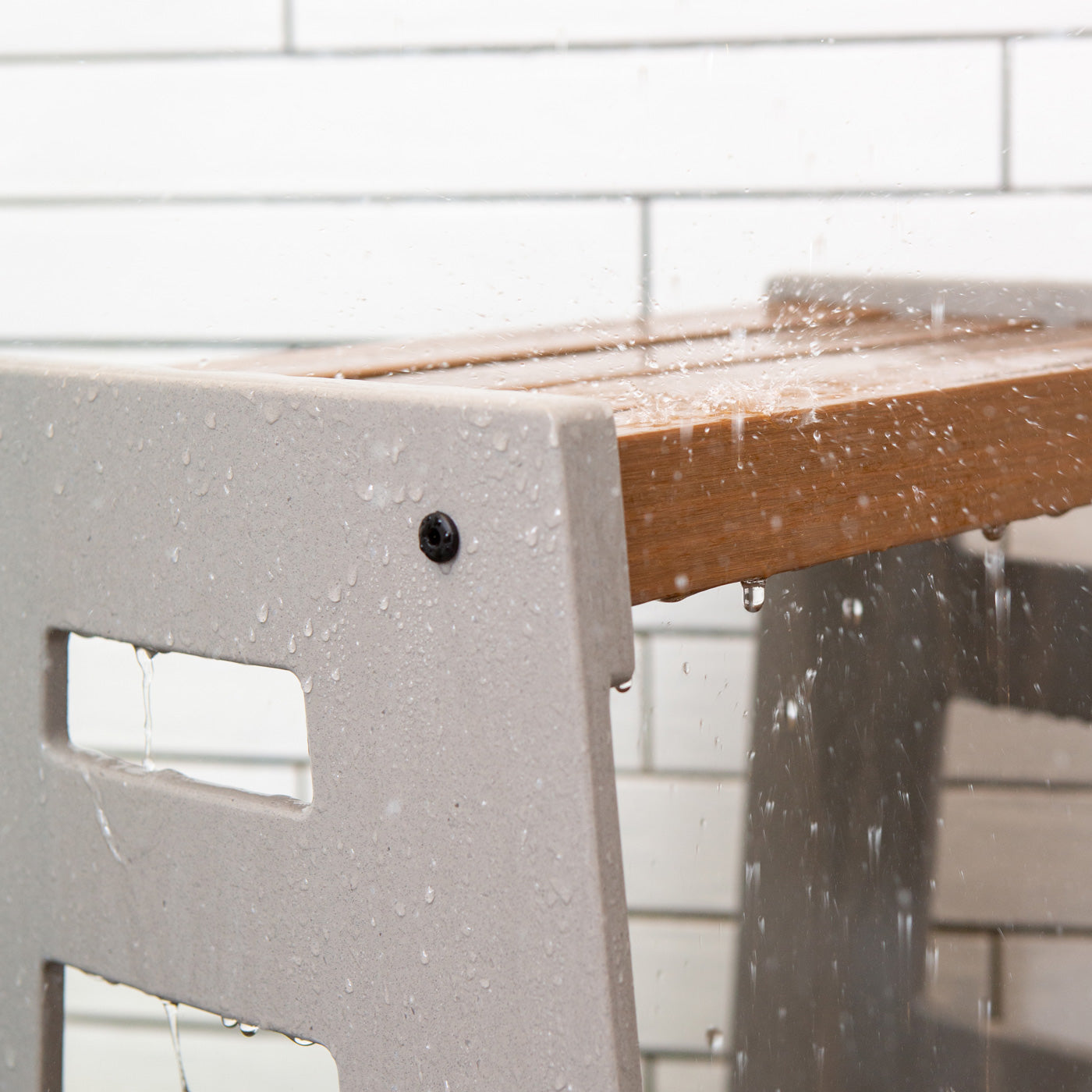 Detail of the Lotic Shower Seat in concrete grey with water falling on the grey solid surface sides and wood composite seat.