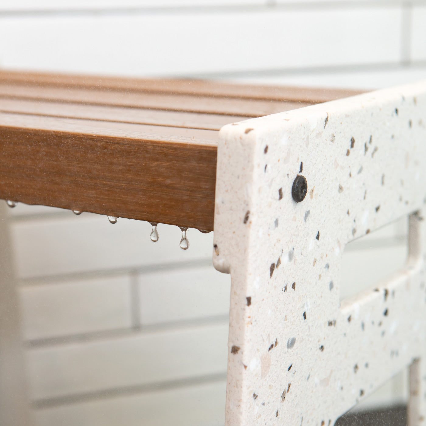 Detail of the Lotic Shower Seat in terrazo that shows water dripping off the wood composite seat and the terrazzo solid surface sides.