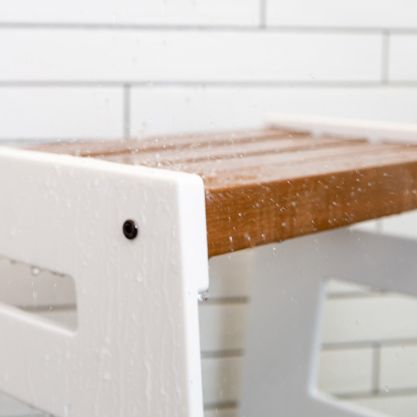 Close-up of the Lotic Shower Seat in white with water falling on the white solid surface sizes and wood composite seat.