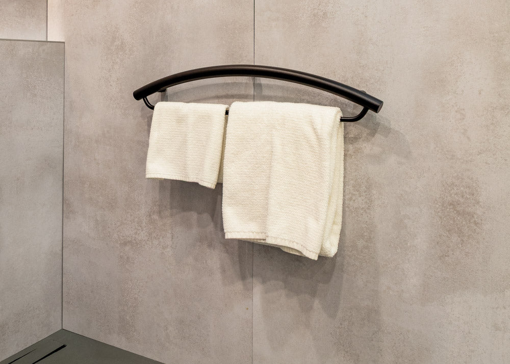 Two white towels hanging on a black towel rack and grab bar combination against a tiled wall.