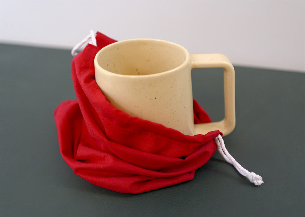 cream ceramic mug with a large handle inside a red cloth on a green surface.